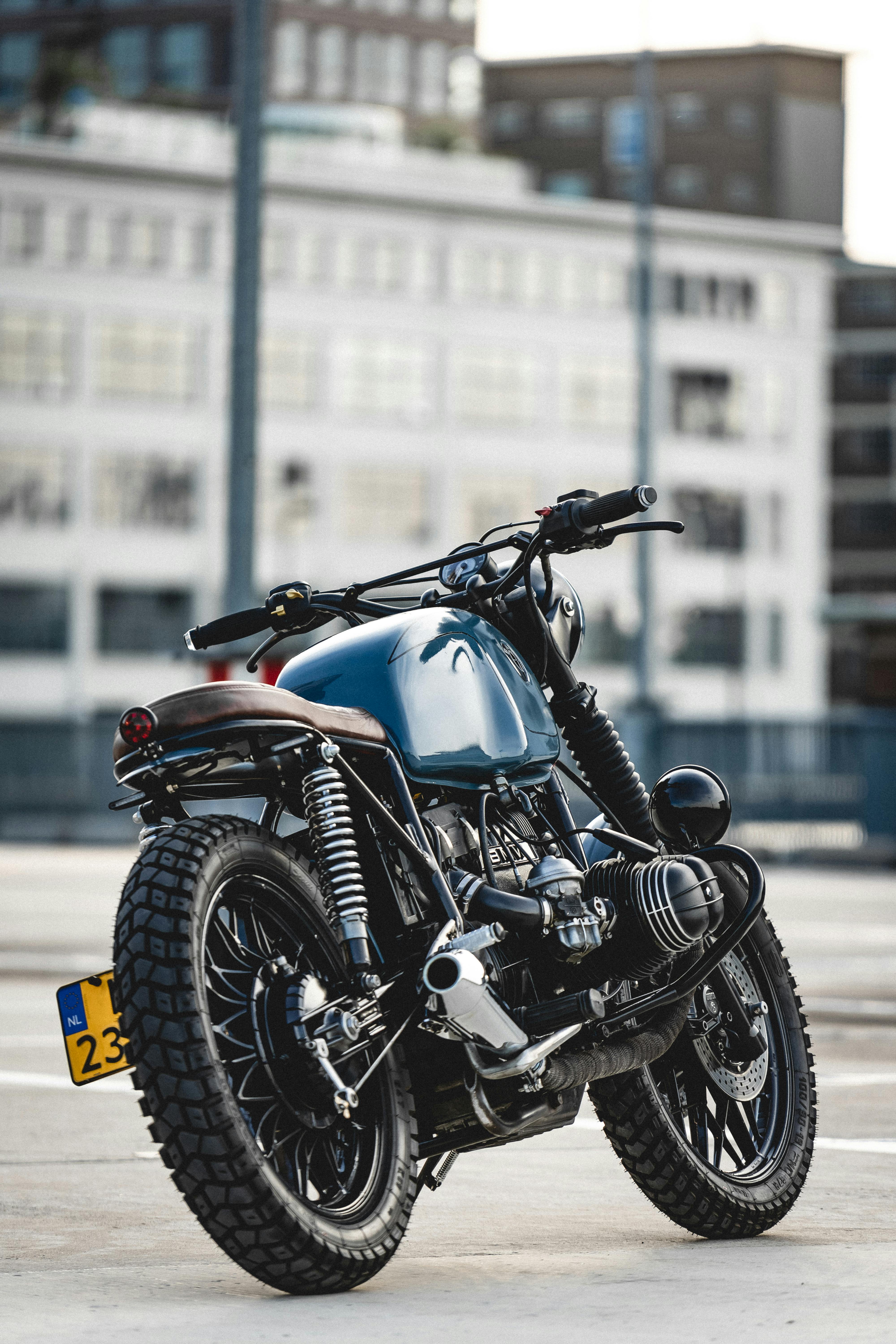 Motocicleta customizada de estilo vintage azul estacionada em frente a um prédio moderno.
